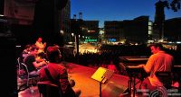 Band auf rot beleuchteter Bühne mit Publikum und Stadt im Hintergrund, es ist Nacht geworden, Quelle: DTF