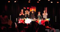 drei Frauen und zwei Männer stehend und sitzend an einem dicht bedeckten roten Tisch mit Länderflaggen vor SIlhouette des Publikums, Quelle: DTF