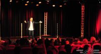 Mann im schwarzen Sakko spricht gestikulierend auf der Bühne vor Publikum, Quelle: DTF
