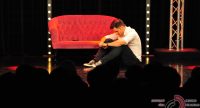 Mann sitzend auf der Bühne vor dem roten Sofa vor Silhouette des Publikums, Quelle: DTF