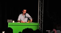 Mann sitzt am grünen Schreibtisch vor Silhouette des Publikums, Quelle: DTF
