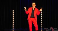 Mann im roten Anzug spricht gestikulierend auf der Bühne vor Silhouette des Publikums, Quelle: DTF