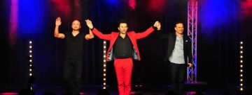 vier Männer tanzend auf der Bühne mit erhobenen Armen vor Silhouette des Publikums