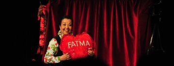 ältere Frau hält lächelnd ein rotes Herzförmiges Kissen mit dem Namen Fatma in die Luft