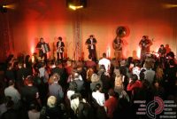 Band auf rot beleuchteter Bühne vor tanzenden Menschen, Quelle: DTF