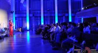 Mann im roten Anzug auf blau beleuchteter Bühne vor Silhouette des Publikums, Quelle: DTF