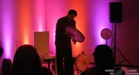 Mann mit Tamburine auf rot beleuchteter Bühne vor Silhouette des Publikums, Quelle: DTF