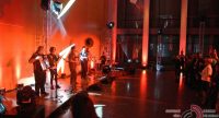 Band auf rot beleuchteter Bühne vor stehenden Menschen, Quelle: DTF