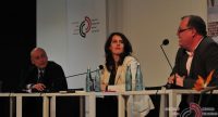 zwei Männer und eine Frau sitzen an Holztischen vor Banner des DTF, Quelle: DTF