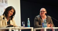 Mann und Frau sitzend an Holztischen, vor ihnen stehen Wasserflaschen, Quelle: DTF
