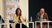 Mann und Frau sitzend an Holztischen, vor ihnen stehen Wasserflaschen, Quelle: DTF