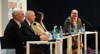 Diskussionsteilnehmer sitzend an Holztischen, vor ihnen stehen Wasserflaschen, Quelle: DTF