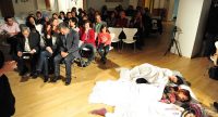 drei junge Frauen liegen in weißen Bettlaken auf dem Boden neben Menschen sitzend auf weißen STühlen, Quelle: DTF