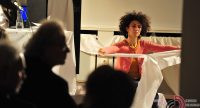Frau mit Afro zerreißt Bettlaken vor Silhouette des Publikums, Quelle: DTF