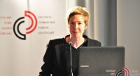 Frau in schwarzem Sakko spricht ins Mikrofon am Rednerpult vor Banner des DTF, Quelle: DTF