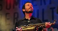Saxophonist hält sein Instrument in den Händen und schaut nach oben rechts, Quelle: DTF
