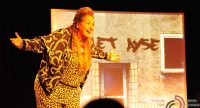 Frau in Anzug mit Leopardprint steht auf der Bühne vor SIlhouette des Publikums, Quelle: DTF