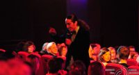 Mann mit langen Haaren im dunkelvioletten Sakko läuft durchs rot beleuchtete Publikum, Quelle: DTF