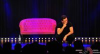 Mann im schwarzen Shirt hockt vor einem pinken SOfa auf der Bühne vor SIlhouette des Publikums, Quelle: DTF