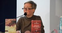Frau in braunem Pullover spricht ins Mikrofon, neben ihr sind zwei Bücher hochkant aufgestellt, Quelle: DTF