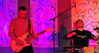 Gitarrist und Schlagzeuger auf violett beleuchteter Bühne, Quelle: DTF