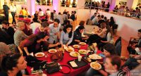 Menschen sitzend rund um einen roten Tisch mit Tellern voller Essen vor sich, Quelle: DTF