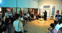 Menschen im Sitzkreis hören einer sprechenden Frau in einem Ausstellungsraum zu, Quelle: DTF