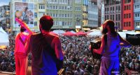 drei Musiker werden von hinten rot und blau beleuchtet, das Publikum im Bildhintergrund, Quelle: DTF