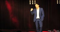 Mann im blauen Anzug auf rot beleuchteter Bühne vor Silhouette des Publikums, Quelle: DTF