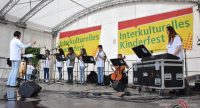 Band in weißen Shirts mit DIrigent spielt auf Bühne vor Banner des Kinderfests, Quelle: DTF