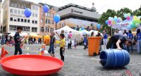 rumwuselnde Menschen auf dem Marktplatz mit Luftballons und bunten Gegenständen, Quelle: DTF