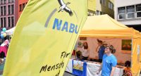 Junger Mann in blauem Shirt neben gelbem Banner des Nabu, Quelle: DTF