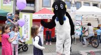 Person in Penguin-Kostüm gibt einem kleinen Mädchen die Hand, daneben stehen ein Vater mit weiteren Mädchen mit Luftballons mit den Händen, Quelle: DTF