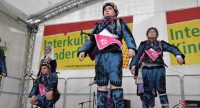 Jungs und Mädchen in traditioneller Kleidung stehen auf der Bühne vor Bannern des Kinderfestes, Quelle: DTF