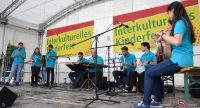 Band in blauen Shirts sitzt und steht spielend auf der Bühne vor Bannern des Kinderfestes, Quelle: DTF