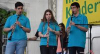 zwei junge Männer und eine junge Frau auf der Bühne neben Banner des Kinderfestes spielen Klarinette, Quelle: DTF