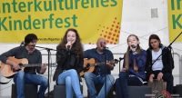 sitzende Band mit zwei Sängerinnen auf der Bühne vor Banner des Kinderfestes, Quelle: DTF