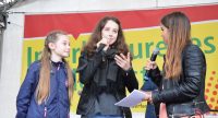 drei stehende junge Frauen auf der Bühne vor Banner des Kinderfestes sprechen ins Mikrofon, Quelle: DTF