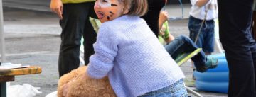 ein geschminktes Mädchen lehnt sich an einem Kuscheltier