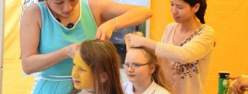 Junge Frauen in einem gelben Zelt flechten das Haar anderer junger Frauen