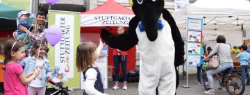Person in Penguin-Kostüm gibt einem kleinen Mädchen die Hand, daneben stehen ein Vater mit weiteren Mädchen mit Luftballons mit den Händen