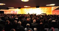 Saal voller Menschen mit hell erleuchtetem Podium im Bildhintergrund, Quelle: DTF