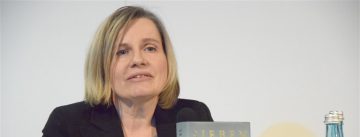 blonde Frau hält lächelnd das Cover eines Buches in die Kamera, rechts neben ihr steht eine Wasserflasche