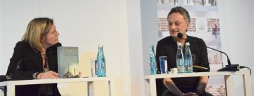 Mann und Frau sitzend sprechen an weißen Holztischen miteinander