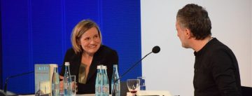 Mann und Frau auf weiß blauem Hintergrund sprechen an weißen Holztischen miteinander