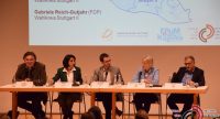 Diskussionteilnehmer sitzend am langen Tisch unter Projektion einer Karte, unter ihnen das Publikum, Quelle: DTF