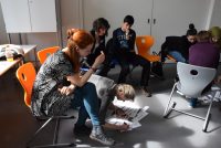 junge Menschen sitzen auf Plastikstühlen, eine junge Frau beugt sich auf den Boden runter, um auf einem Plakat zu schreiben, Quelle: DTF