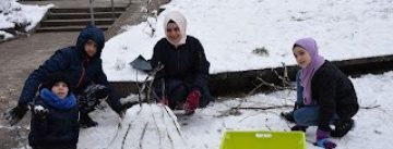 zwei Frauen und zwei Jungs bauen etwas mit Schnee und Äste, sie sind winterlich angezogen