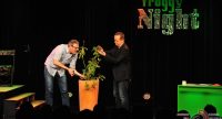 zwei Männer stutzen die Blätter einer grünen Pflanze vor der Silhouette des Publikums, Quelle: DTF