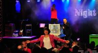 Männer auf der Bühne zeigen auf Frau in roter Jacke welche im Publikum aufgetaucht ist, Quelle: DTF